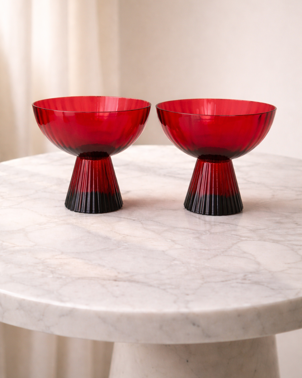 Two red glass bowls with black bases on a marble surface.