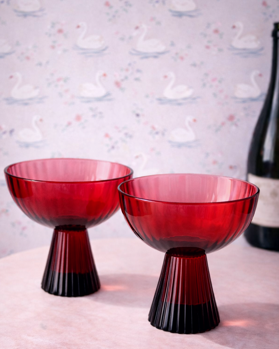 Two red glass bowls with black bases on a white surface with a swan-patterned wallpaper in the background.