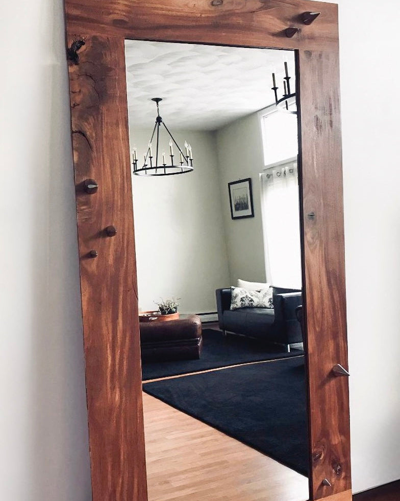 Large wooden-framed mirror on a wall with a room reflection.