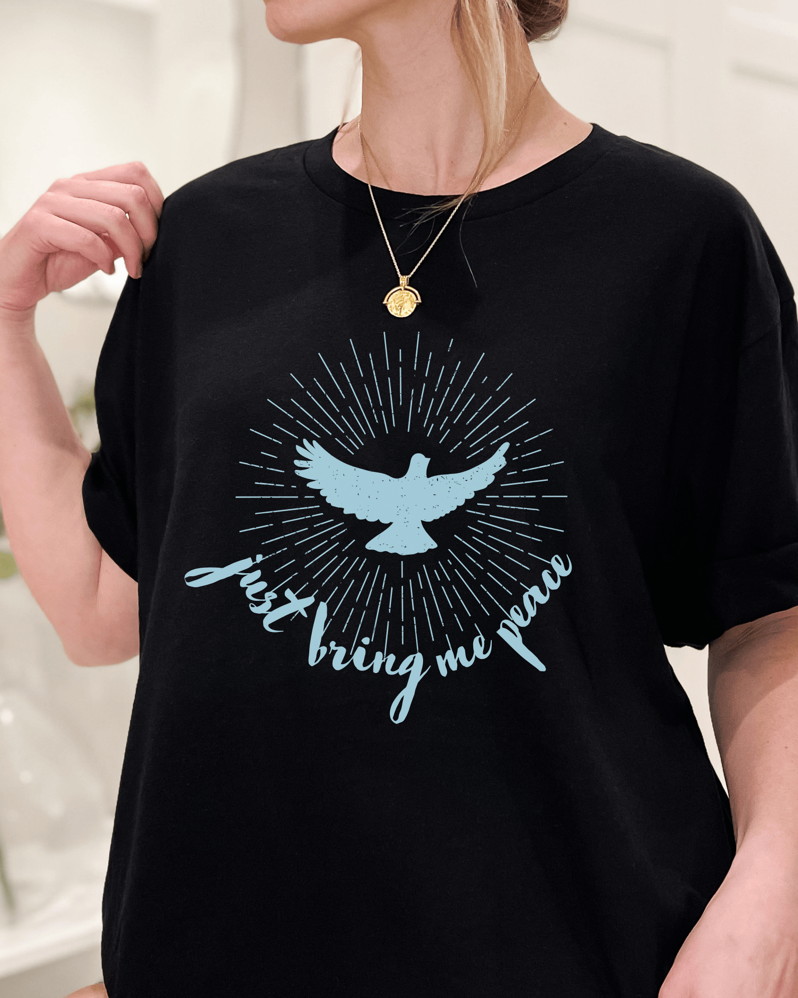 A person wearing a black crew neck t-shirt with a graphic of a blue dove and the text 'Just Bring Me Peace' on the front.