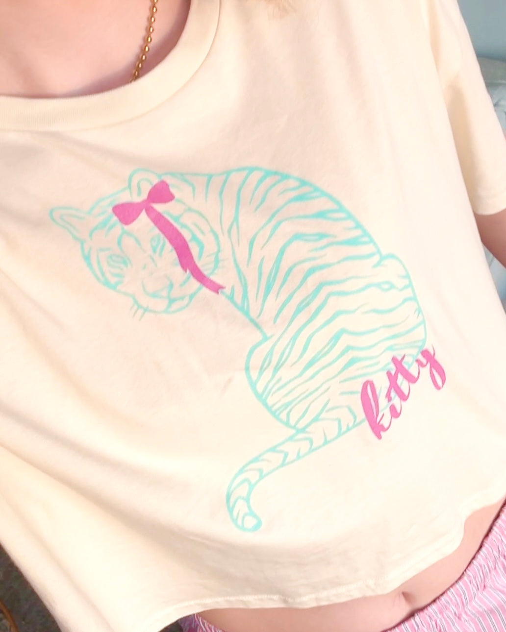 Person wearing a cream-colored t-shirt with a cat graphic and 'fitty' text.