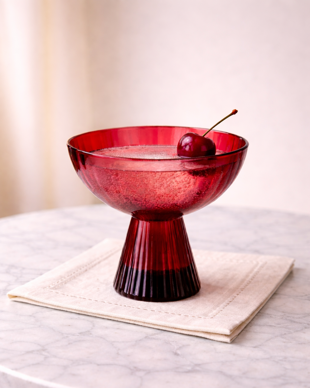 Red glass cocktail glass with a cherry on a marble surface